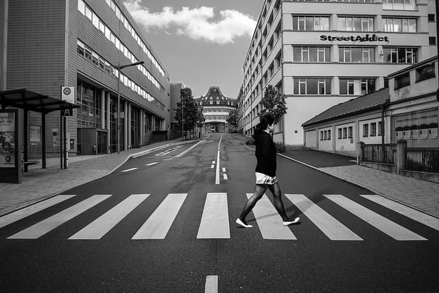 Ein schwarz-weiß Foto einer Person, die auf einem Zebrastreifen eine Straße überquert